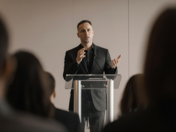 Man speaking on a podium in front of people preview picture