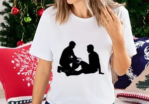 Two men sitting on the ground in silhouette one examining the other's leg
