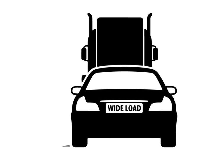 Silhouette of a car with oversized load on a flatbed truck