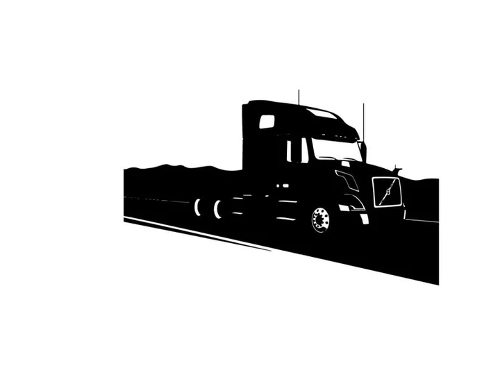 Silhouette of a semi truck driving on a highway with mountains