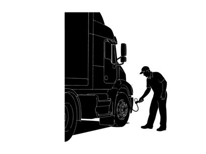Silhouette of a man checking a semi truck tire in a depot